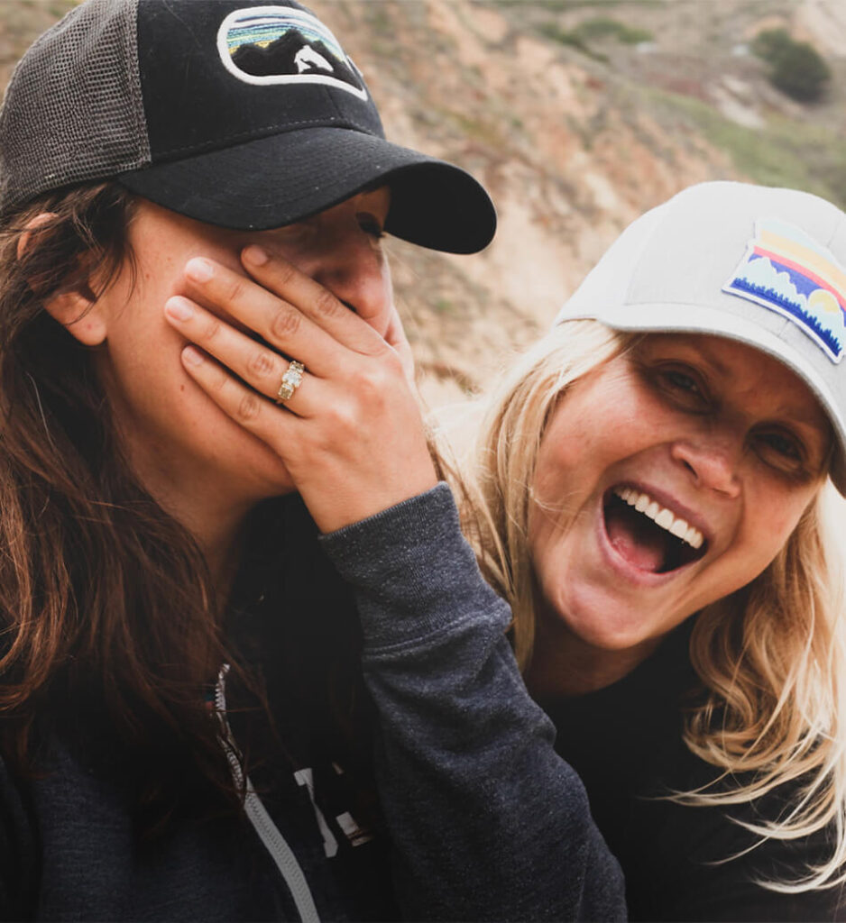 Two queer women laughing together outdoors, representing a joyful LGBTQ+ couple supported through LGBTQ+ matchmaking.