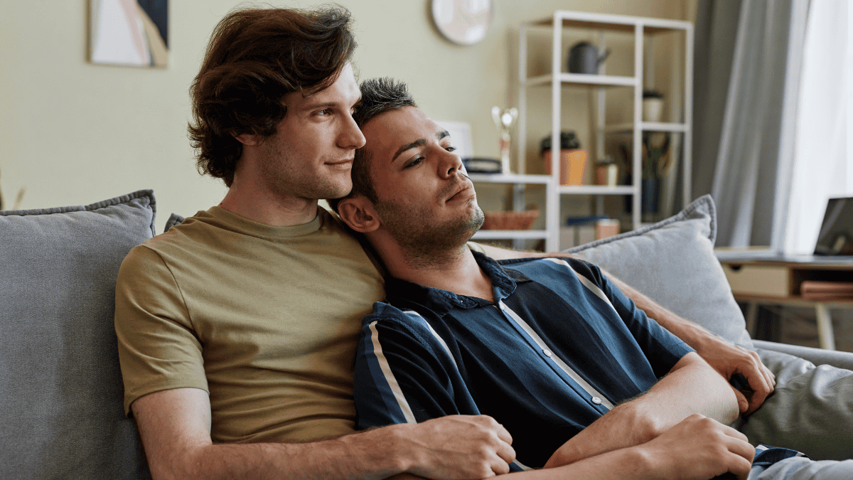 Gay couple relaxing closely together on a couch at home, sharing a quiet and affectionate moment